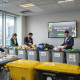 Office staff sorting business waste into recycling bins as screen shows sustainability strategy